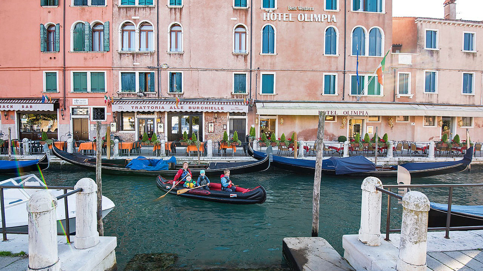 Frau mit 3 Kindern paddelt mit dem aufblasbaren Kanu Adventure in Venedig vor dem Hotel Olimpia